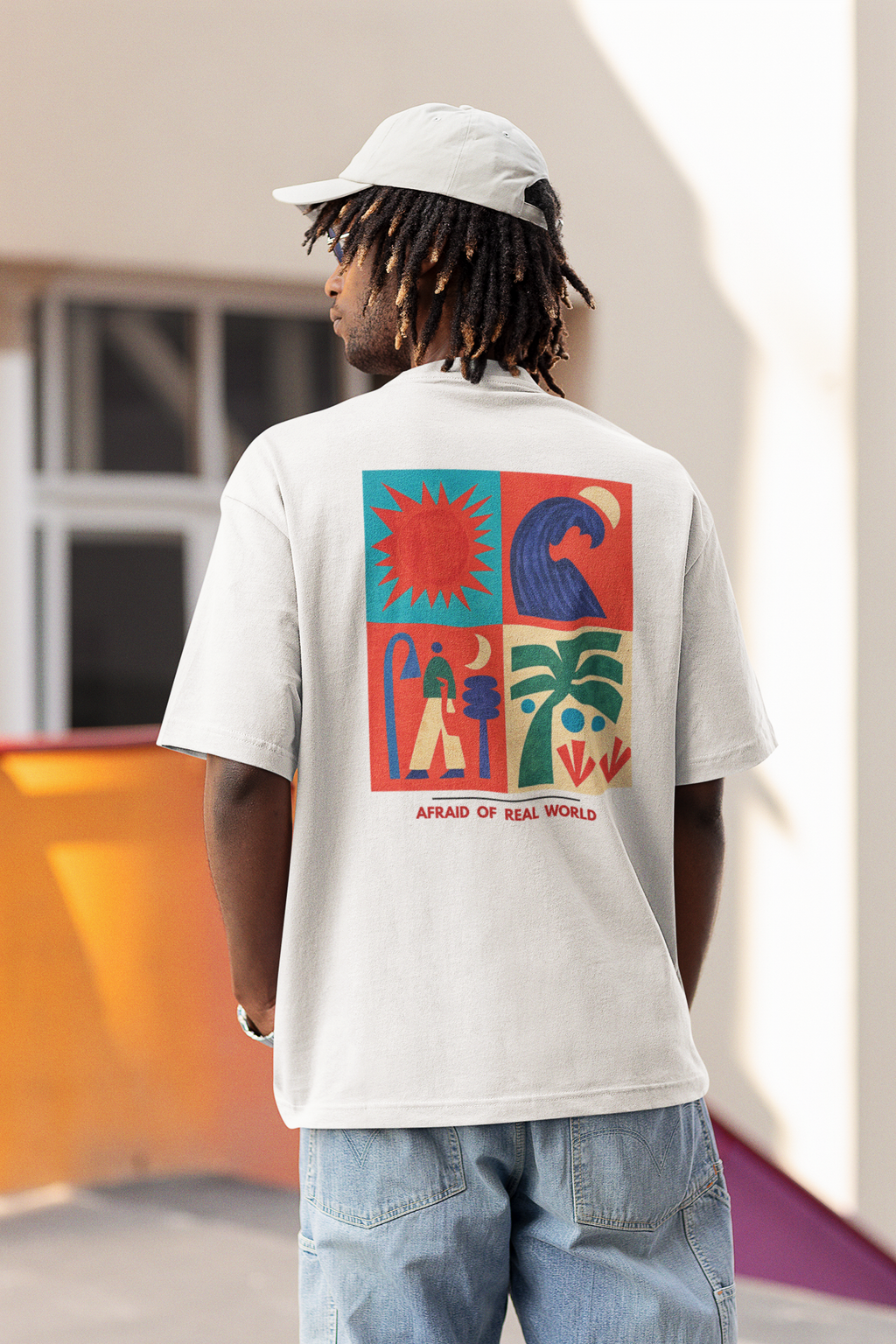 Back view of a man wearing a Pixalflux white oversized t-shirt featuring a colorful four-panel graphic with a sun, ocean wave, and palm tree.